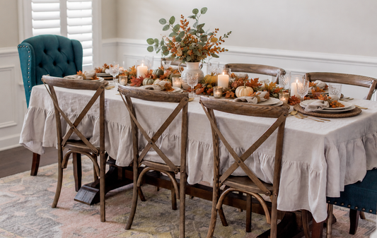 Warm Thanksgiving table layered over an oatmeal linen tablecloth with stoneware, amber glassware and autumn branches