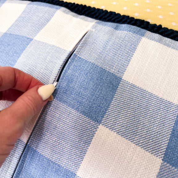 Hand sewing a blue and white checkered fabric with a hand holding a needle.