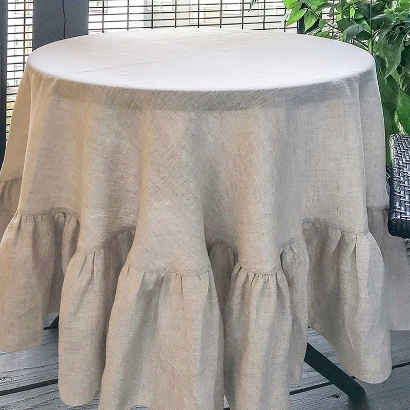 Round table with a beige ruffled tablecloth in an outdoor setting.