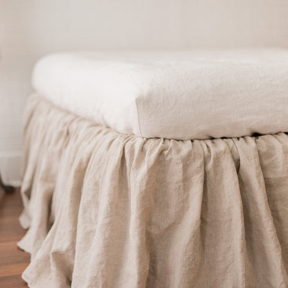 Beige bedskirt on a bed with a white pillow in a room setting.