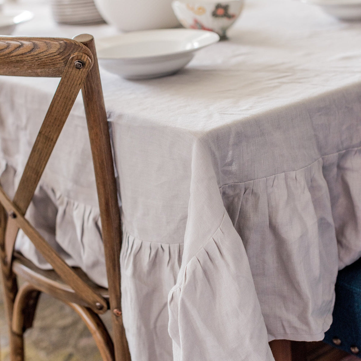 Light gray ruffled tablecloth on a wooden dining table with chairs.