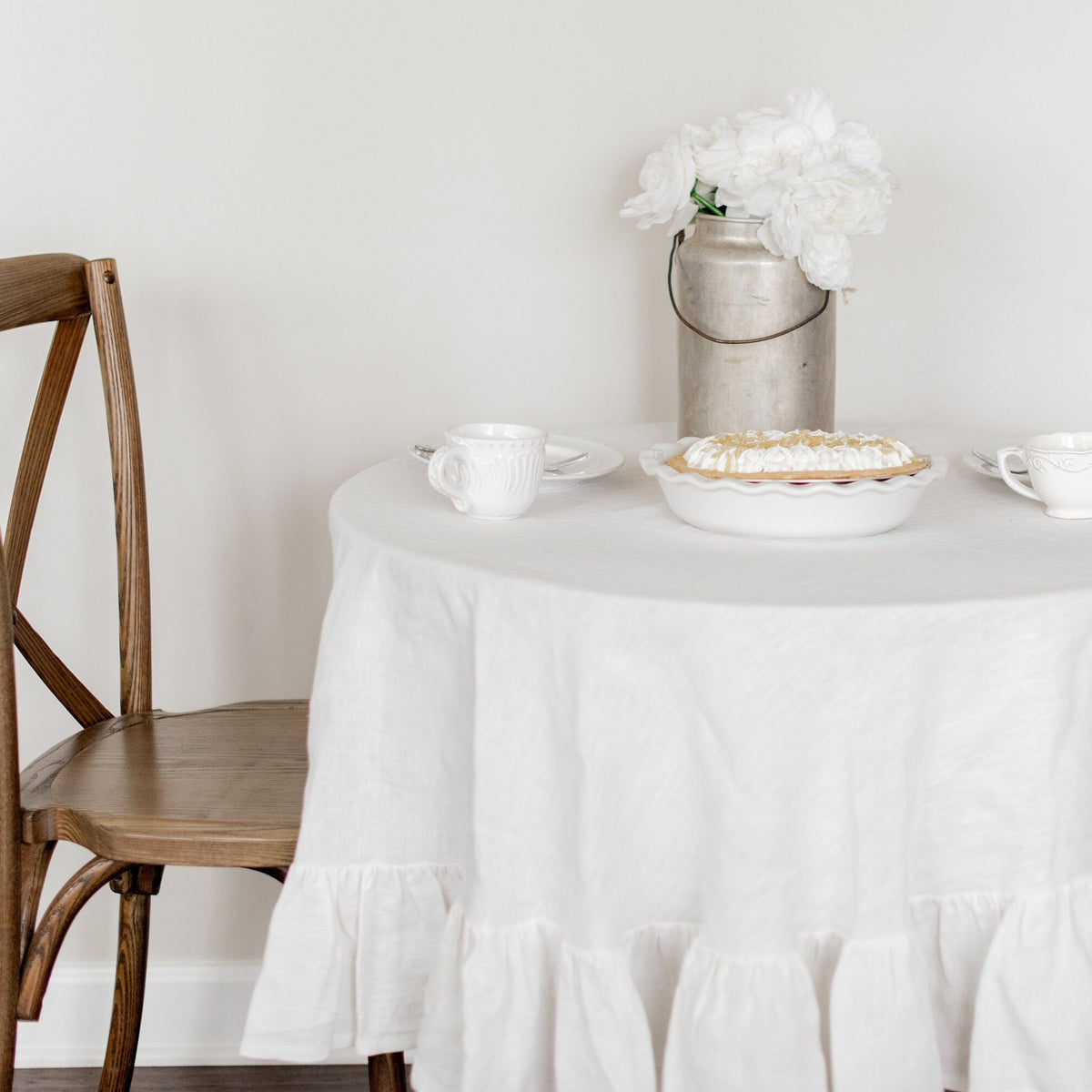 Round table with a white tablecloth, pie, and cups in a minimalistic setting.