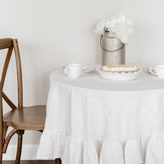 Round table with a white tablecloth, pie, and cups in a minimalistic setting.