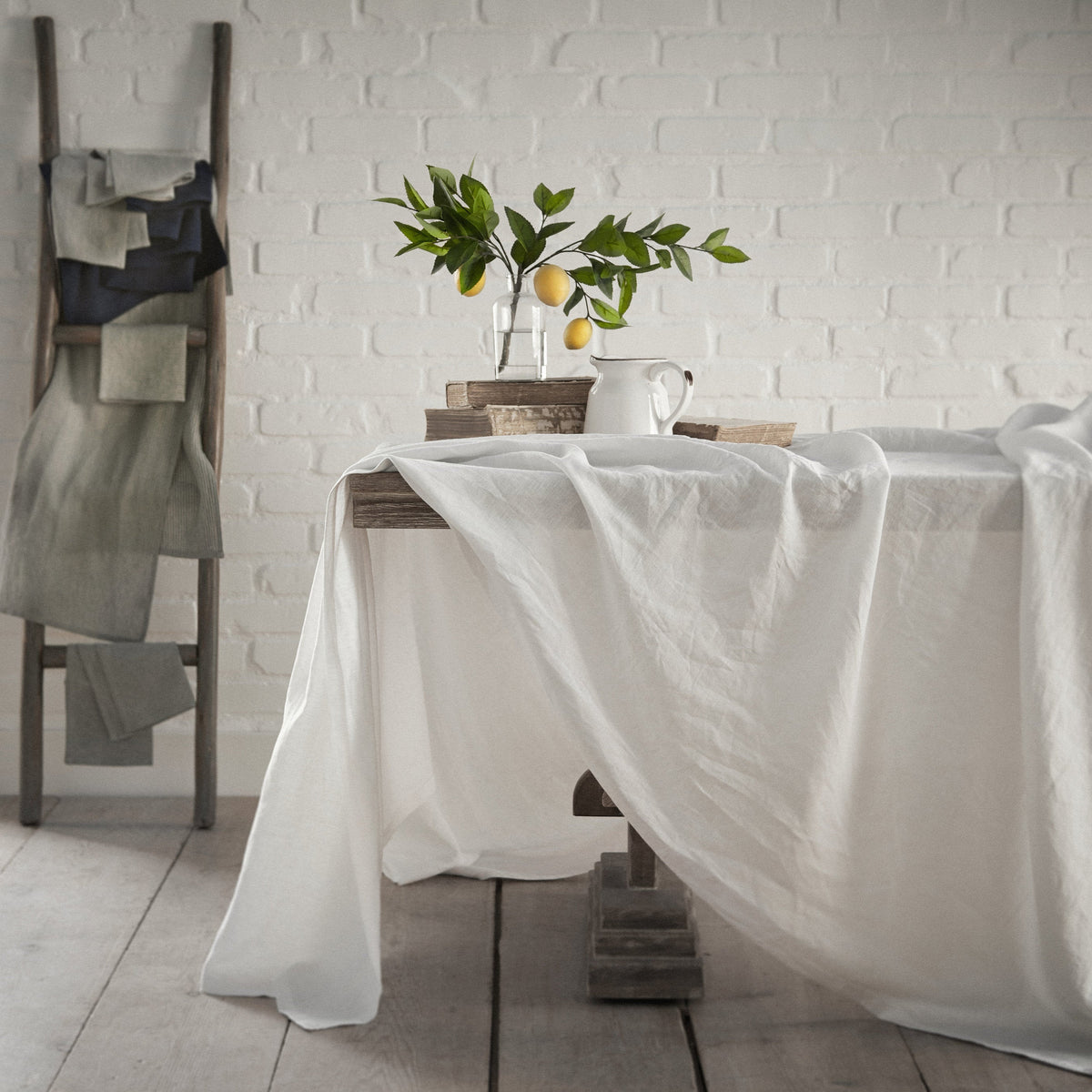 Dining table with a white tablecloth, plant, and decorative items against a white brick wall.