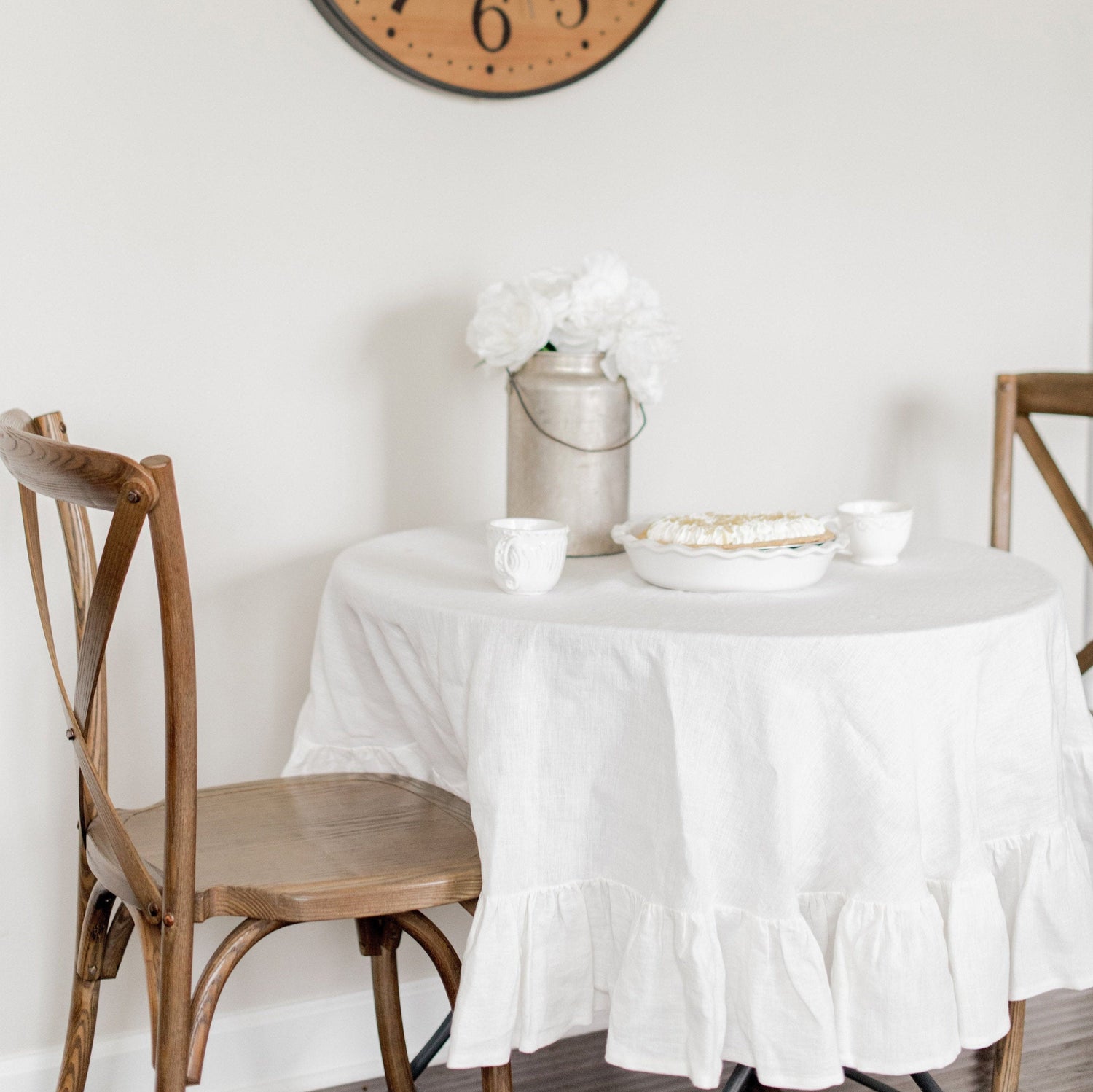 Round table with a white tablecloth, wooden chairs, and decorative items in a room.