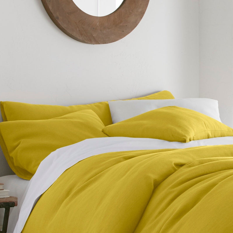 Yellow bedding set on a bed in a bedroom with a lamp and mirror.