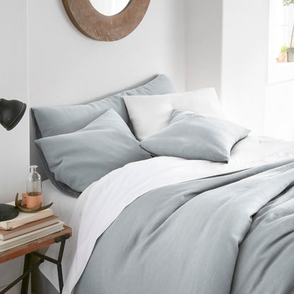 Neatly made bed with light gray bedding in a bedroom setting.