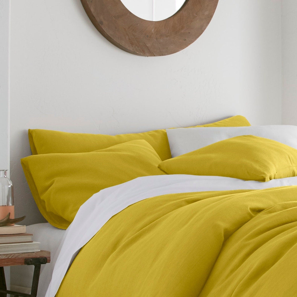 Yellow bedding set on a bed in a bedroom with a lamp and mirror.