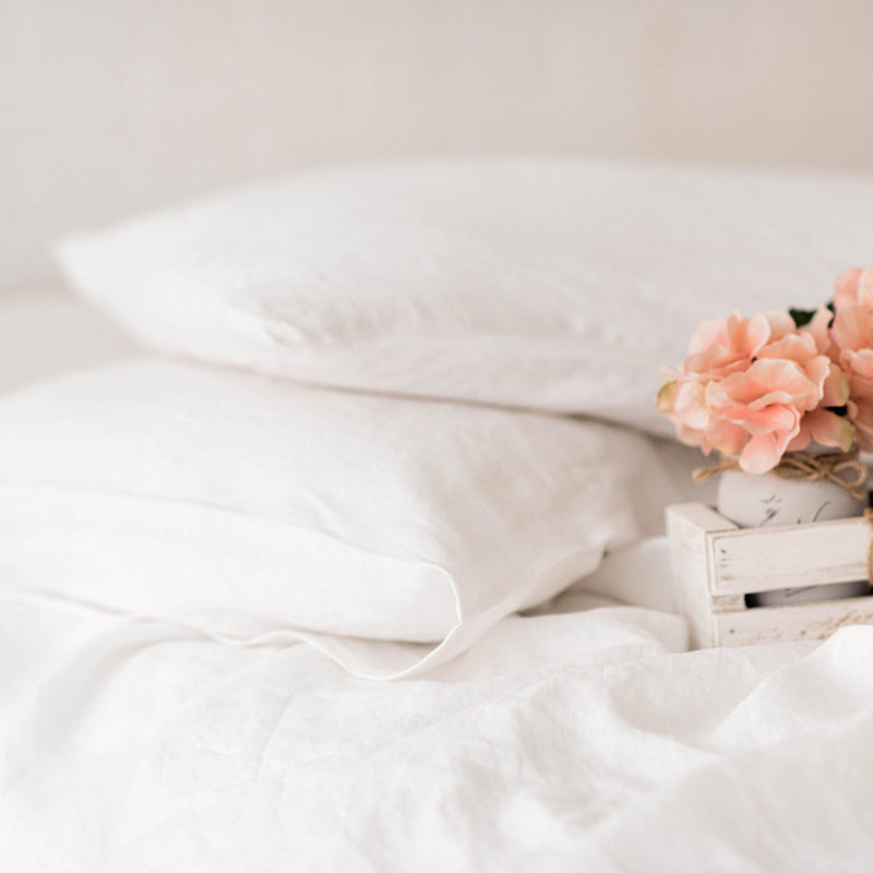 White bedding with a small wooden crate holding pink flowers on a bed.