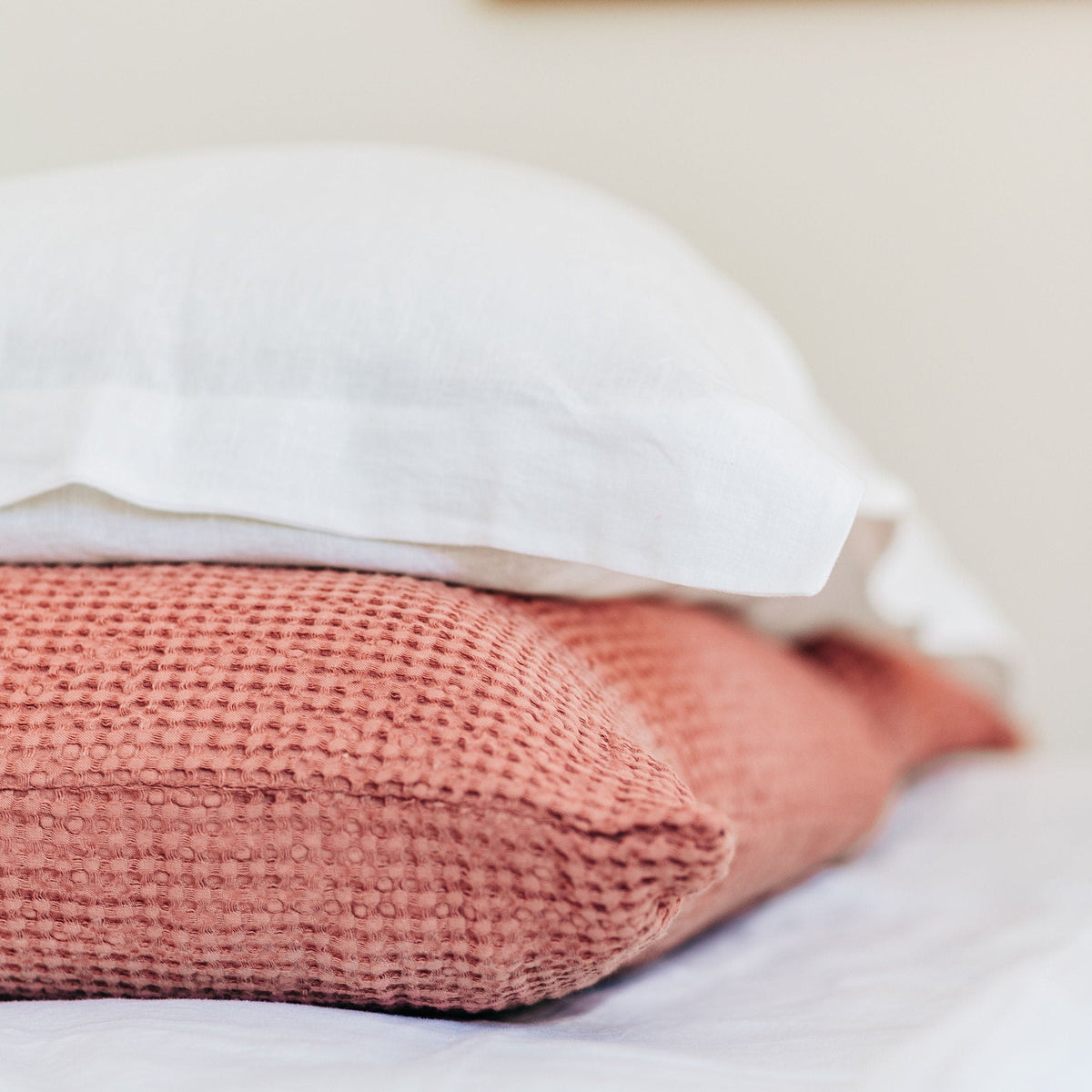 Pink textured throw pillow on a bed with a white pillow