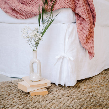 White skirt with a pink knitted throw and a vase with flowers on a beige carpet.
