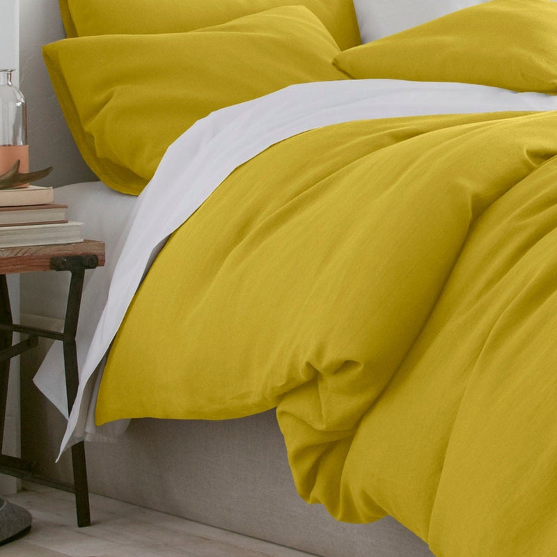 Yellow bedding on a bed with a side table in the background