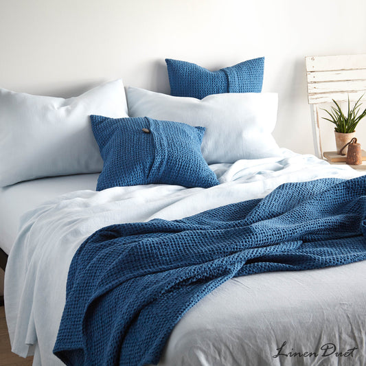 Bed with blue pillows and a blanket in a bright bedroom setting