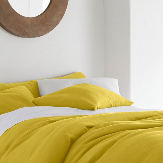 Yellow duvet cover on a bed in a bright bedroom with a mirror and plant.