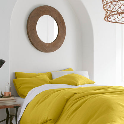 Bedroom with yellow bedding, round wooden mirror, and lamp.