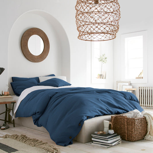 Modern bedroom with blue bedding and a wicker lampshade.