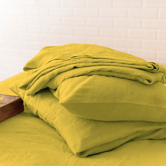 Yellow bedding set on a bed with a wooden tray and vase of flowers.