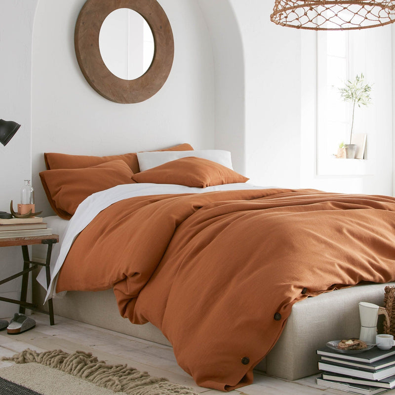 Bedroom with orange bedding and a wicker lampshade.