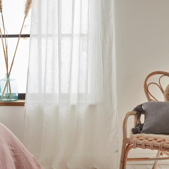 Sheer white curtain in a room with a wicker chair and decorative elements.
