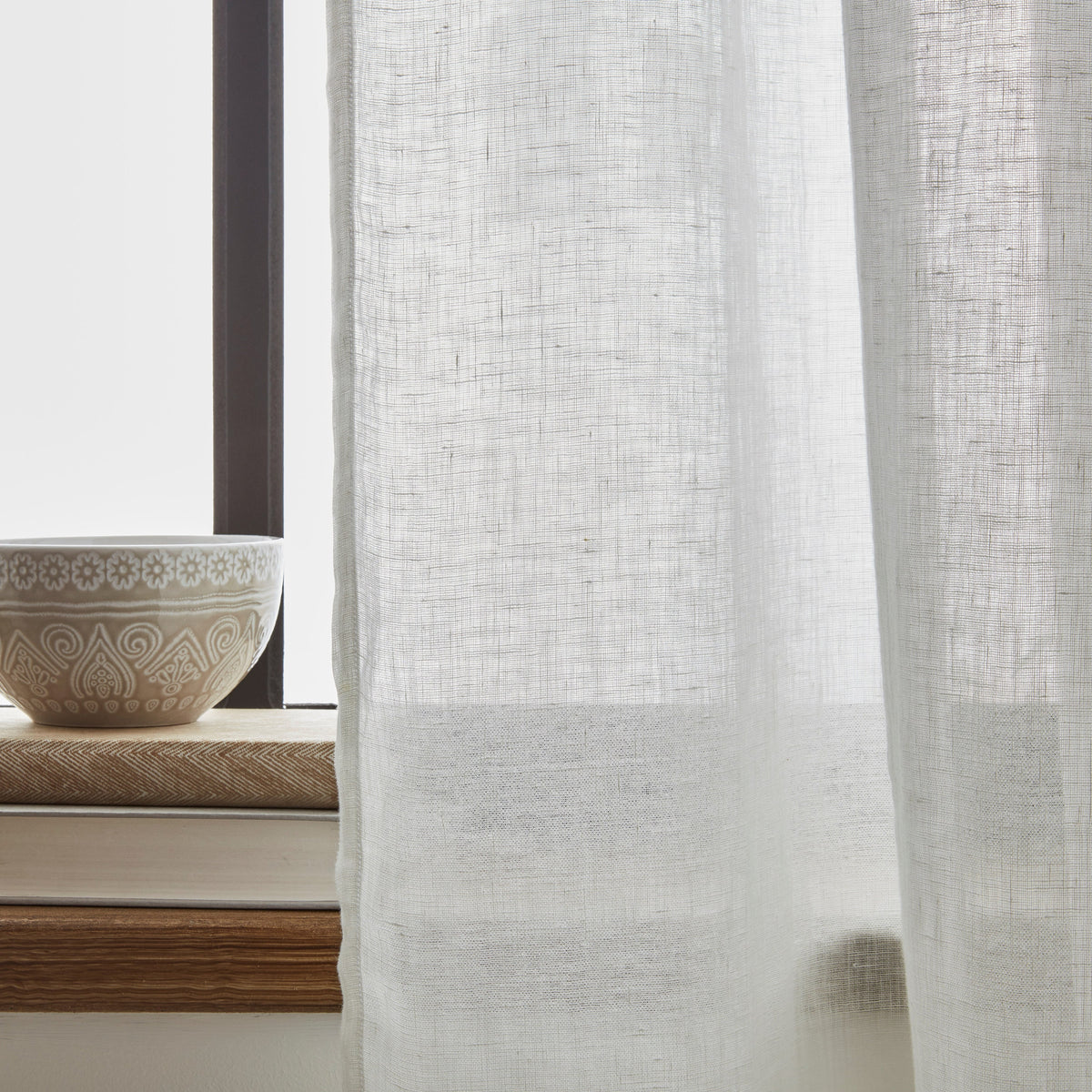 Sheer white curtain with a decorative bowl on a windowsill in the background
