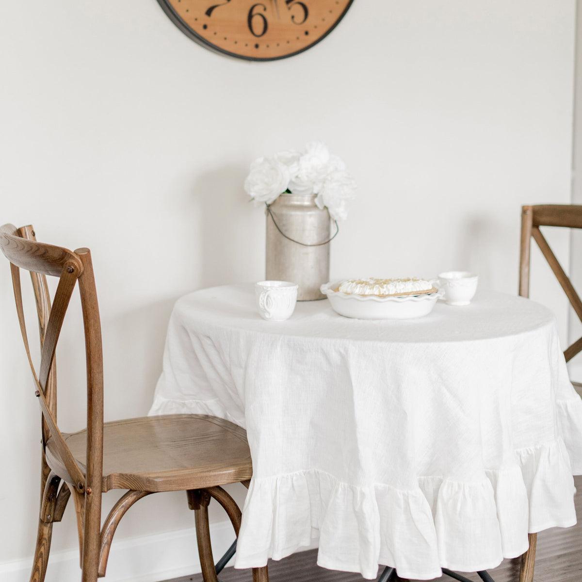 Round table with a white tablecloth, wooden chairs, and decorative items in a room.