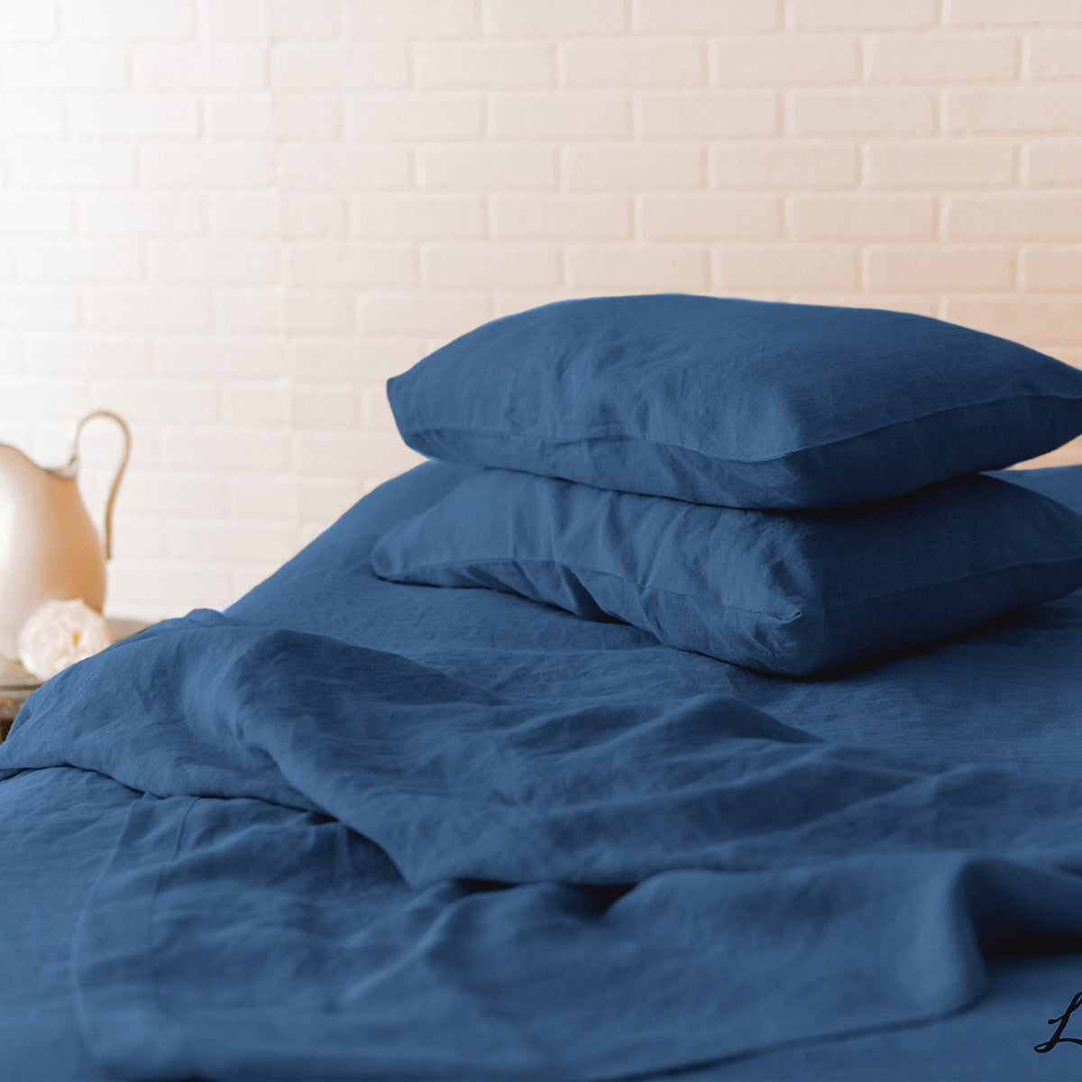 Blue bedding set with pillows on a bed against a white brick wall.