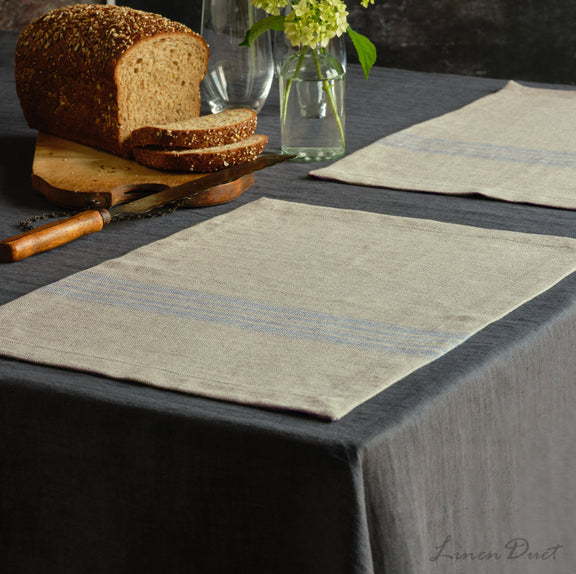 Table setting with striped placemats, bread, and a vase on a dark surface.