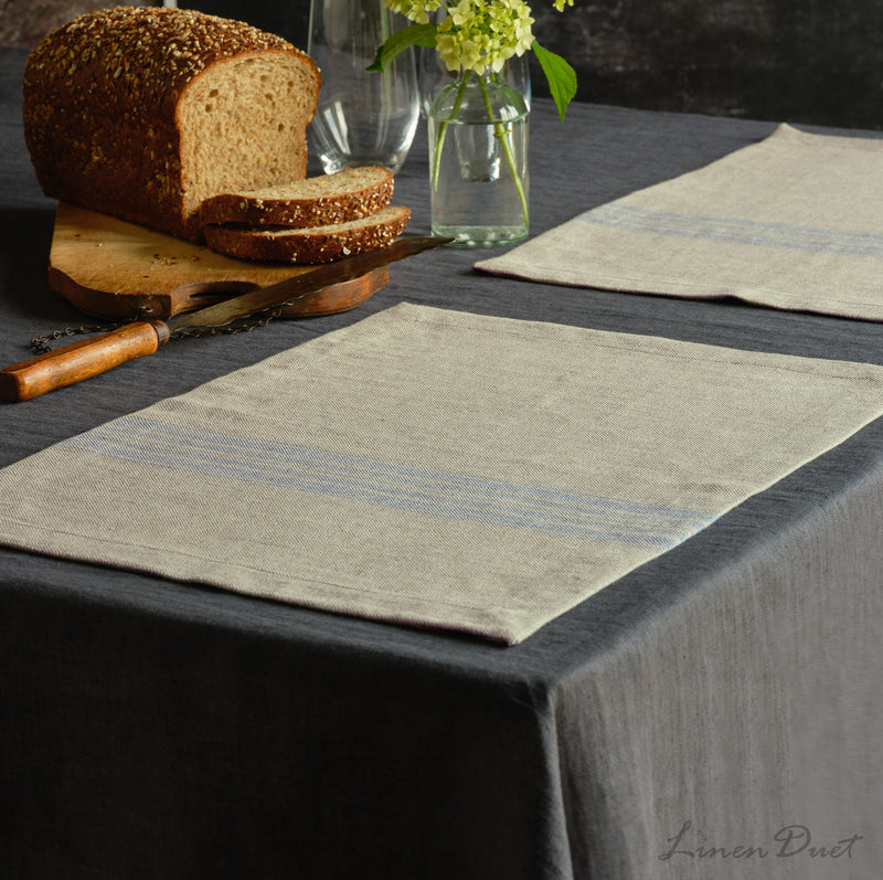 Table setting with striped placemats, bread, and a vase on a dark surface.