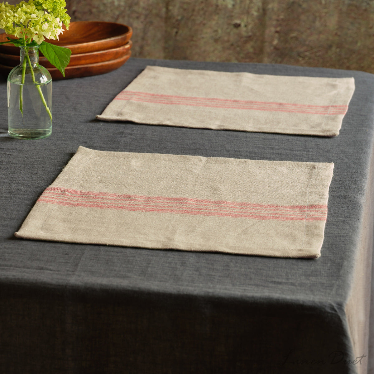 Two striped placemats on a dark tablecloth with a vase of flowers in the background.