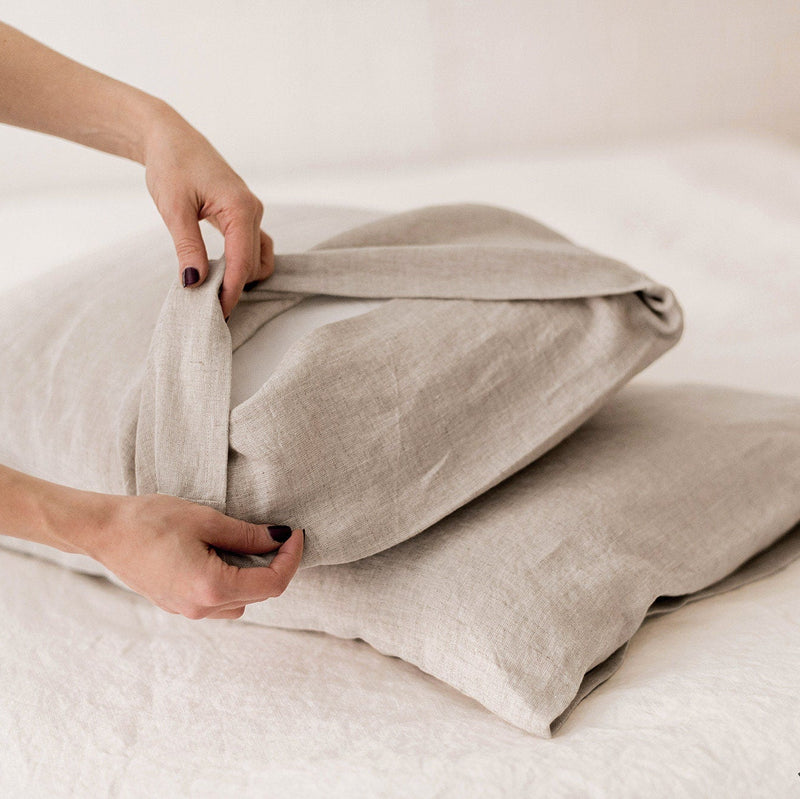 Person folding beige linen pillows on a white bed