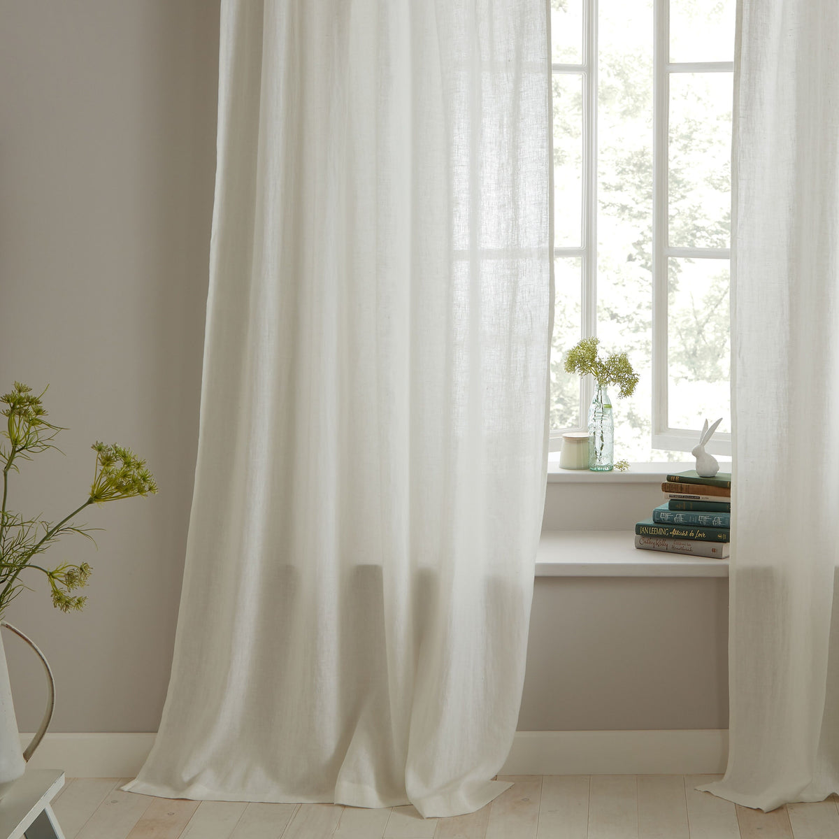 White curtains in a room with a window and books on a windowsill.