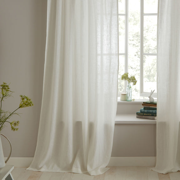 White curtains in a room with a window and books on a windowsill.