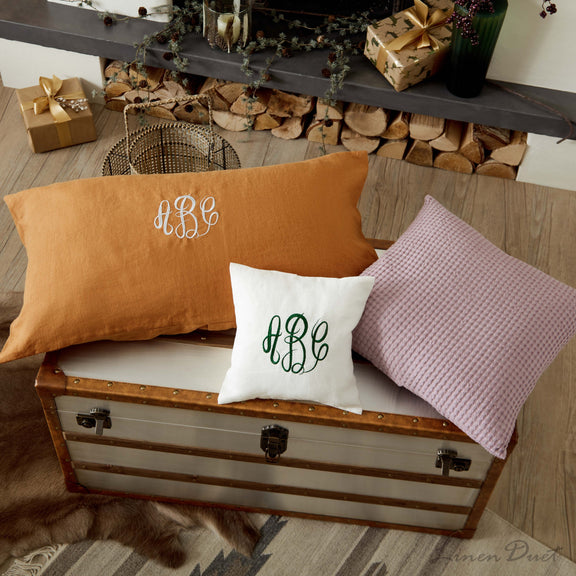 Three pillows with monogram 'HBC' on a wooden chest in a cozy room.