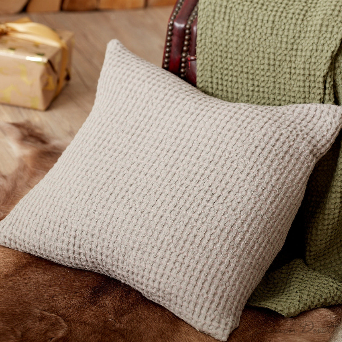 Textured beige pillow on a brown surface with a green blanket