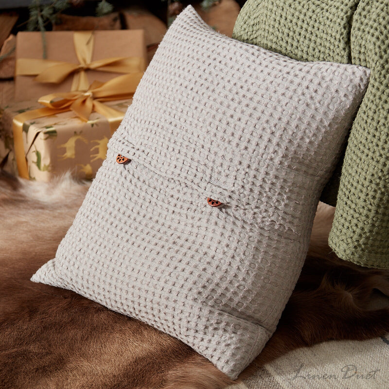 Textured pillow with decorative elements on a fur surface with wrapped gifts in the background