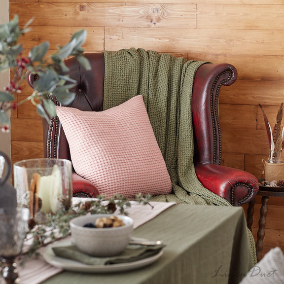 Red leather armchair with pink pillow and green blanket, set against a wooden wall with a table in front.