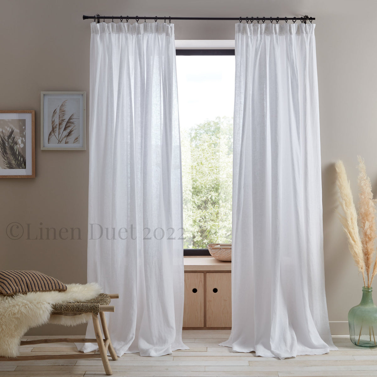White linen curtains in a room with a bench, vase, and window.