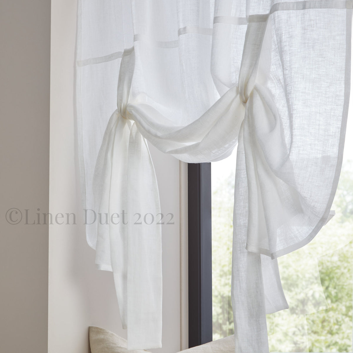 White linen curtain with ruffled edges in a room with a window.