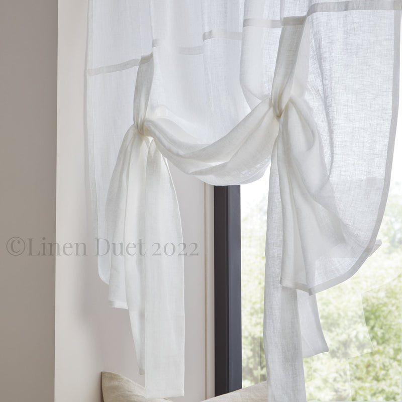 White linen curtain with ruffled edges in a room with a window.