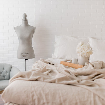 Bedroom with a bed, mannequin, and chair against a white brick wall.