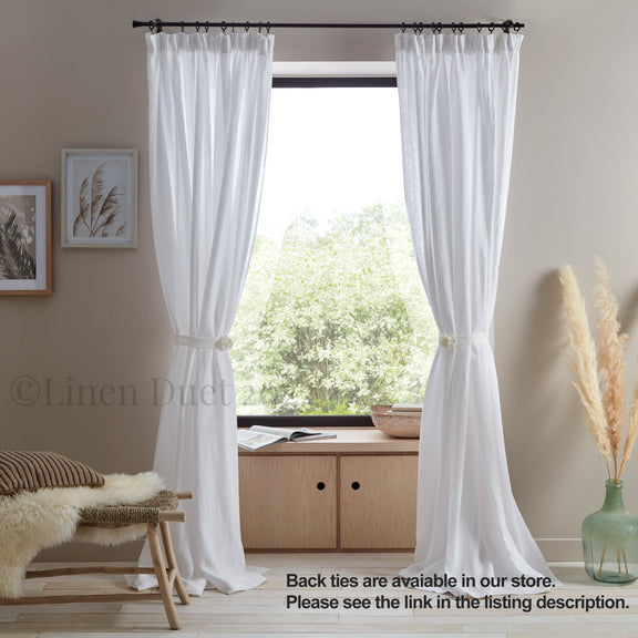 White curtains hanging in a room with a window, wooden cabinet, and decorative items.