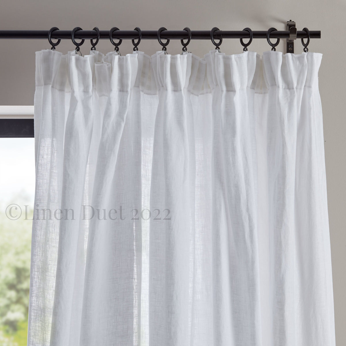 White linen curtain with black rod and hooks on a neutral background
