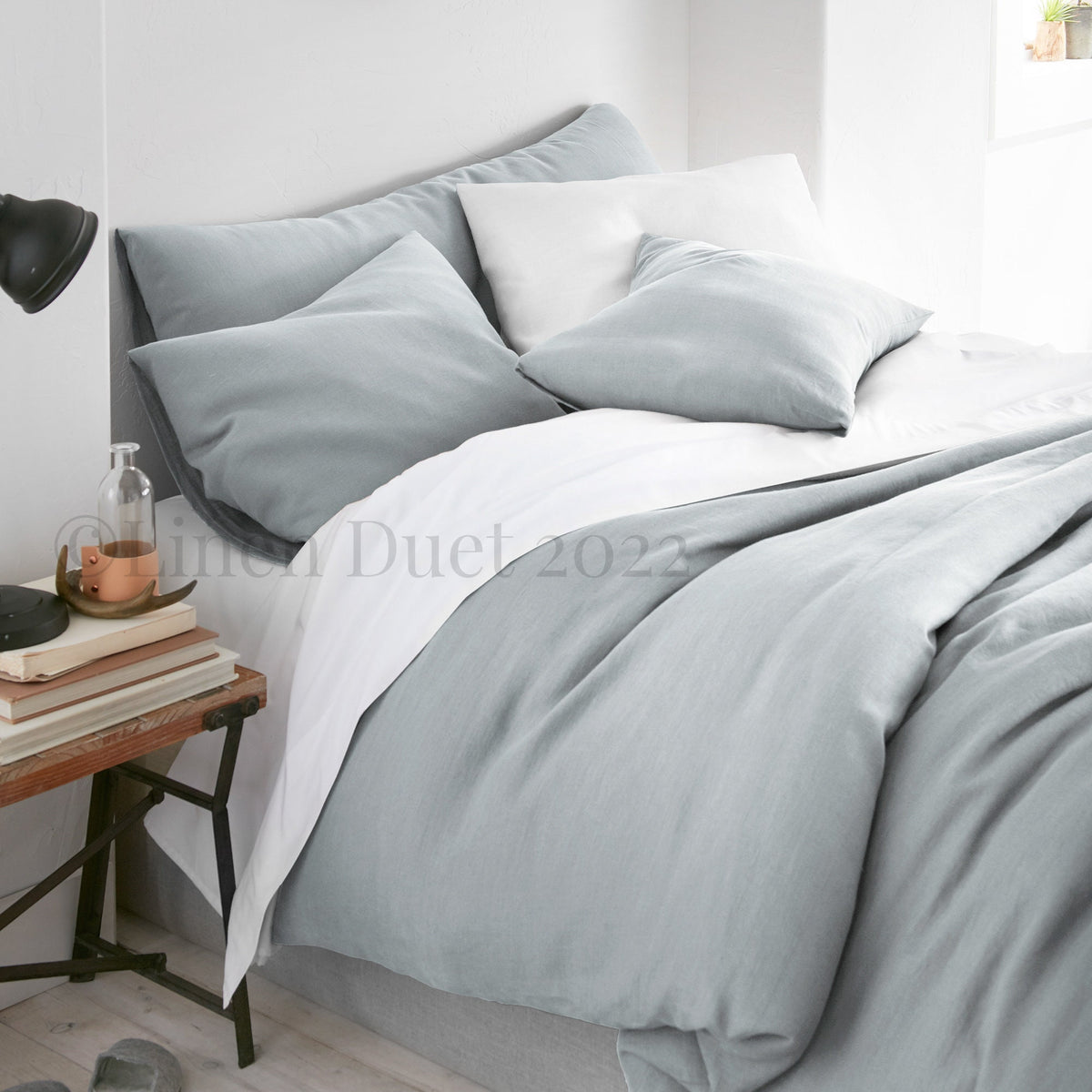Gray bedding set on a bed with a side table in a bedroom setting.