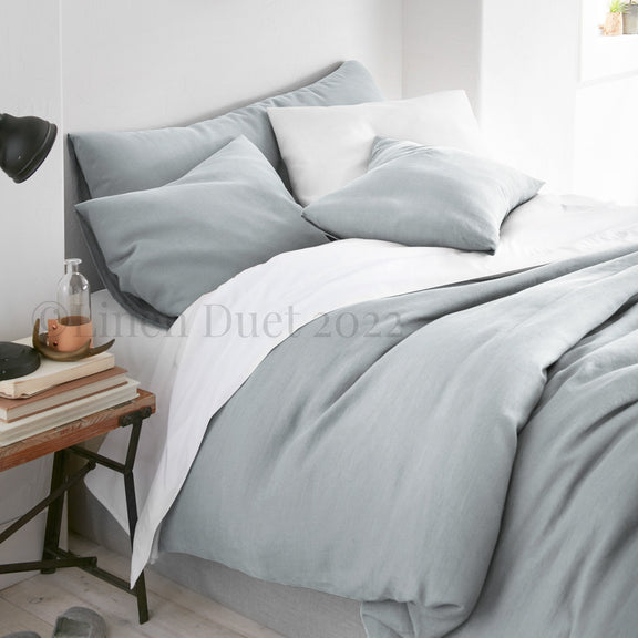 Gray bedding set on a bed with a side table in a bedroom setting.
