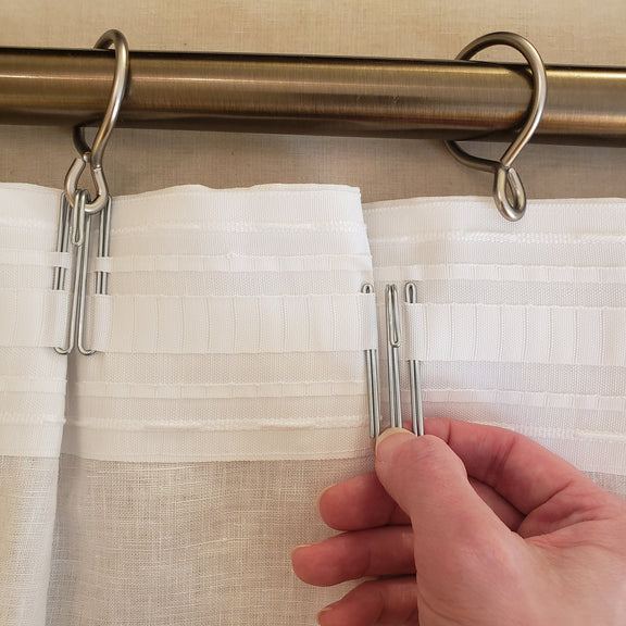 Curtain rod with clips holding white curtains, hand adjusting one clip.
