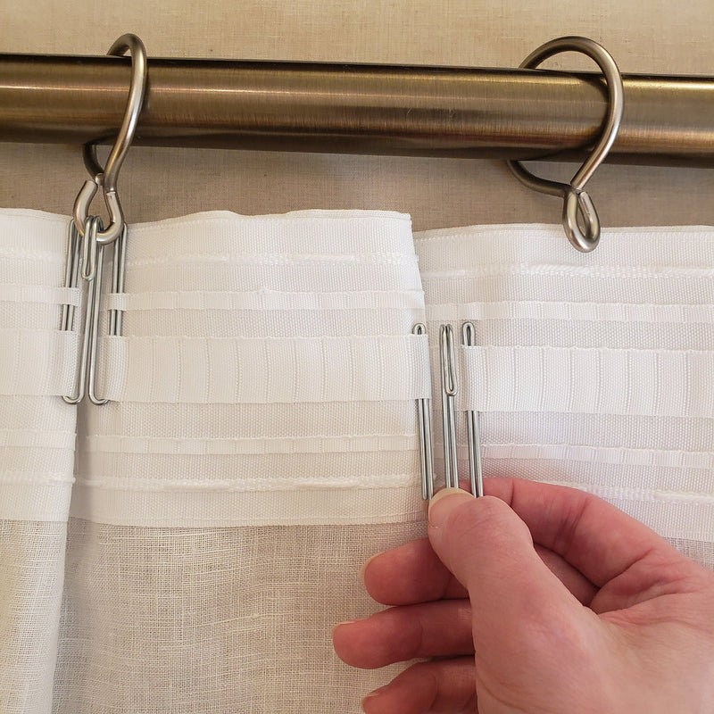 Curtain rod with clips holding white curtains, hand adjusting one clip.