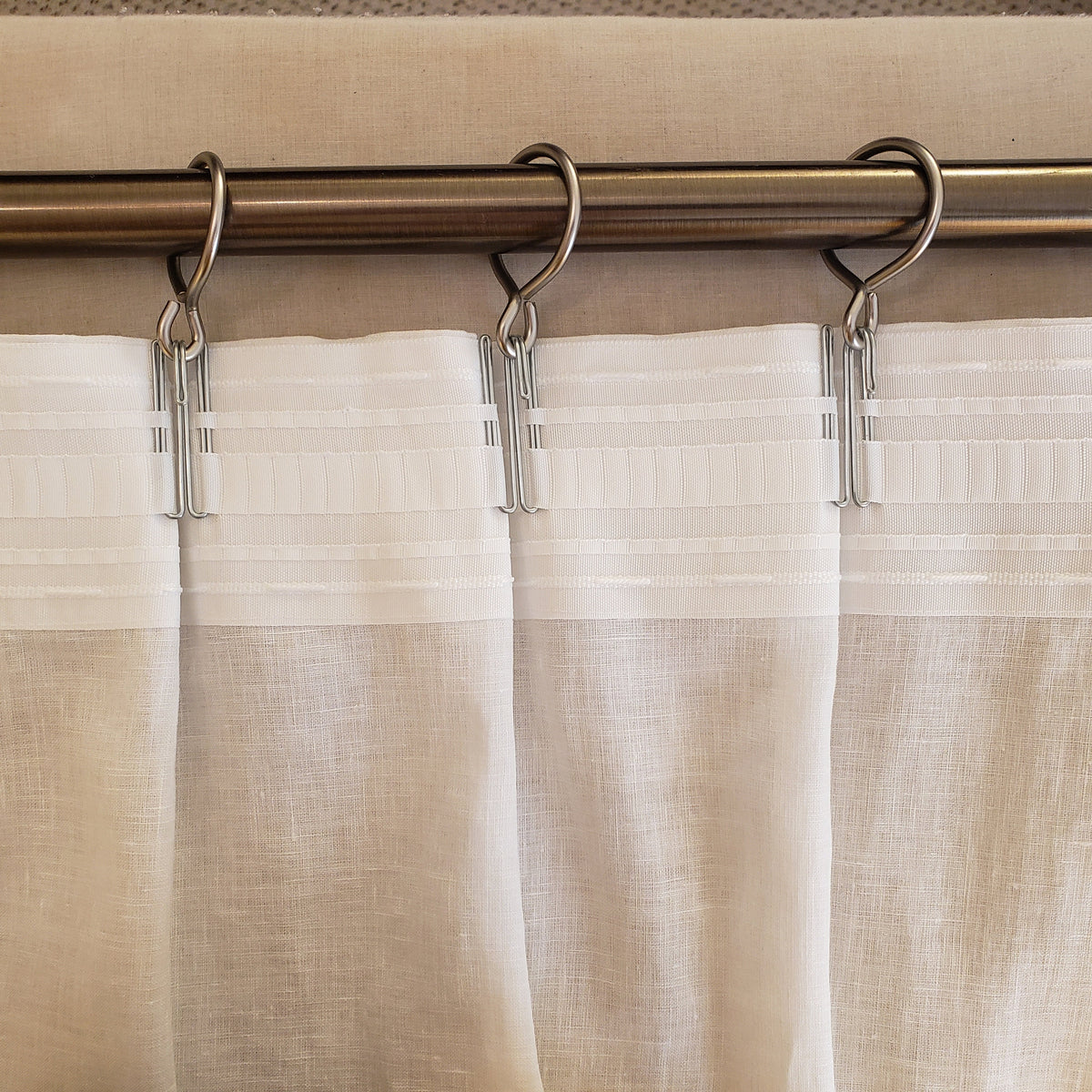 Sheer beige curtains with a rod and hooks in a close-up shot.
