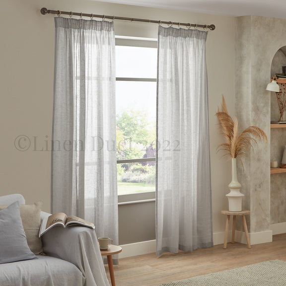 Sheer gray curtains in a living room setting with a couch and decorative elements.