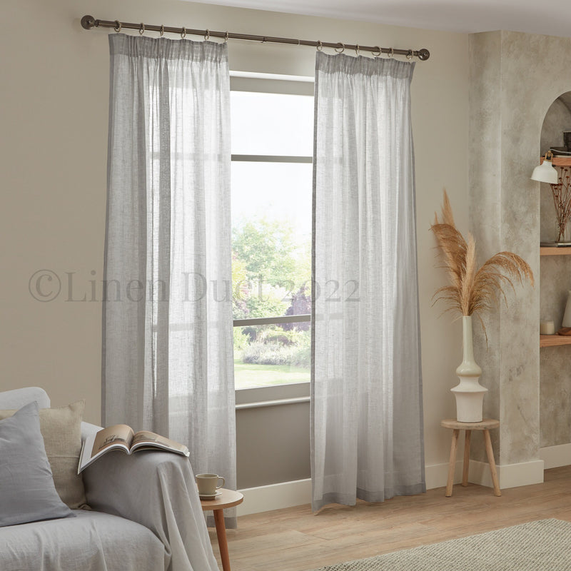Sheer gray curtains in a living room setting with a couch and decorative elements.