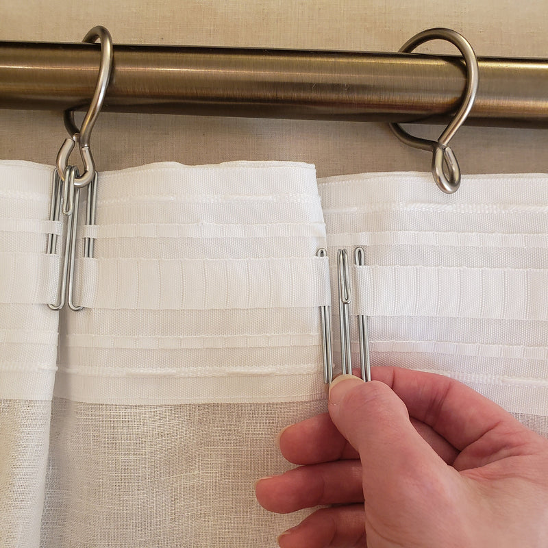 Curtain rod with clips holding a white curtain, with a hand adjusting one of the clips.